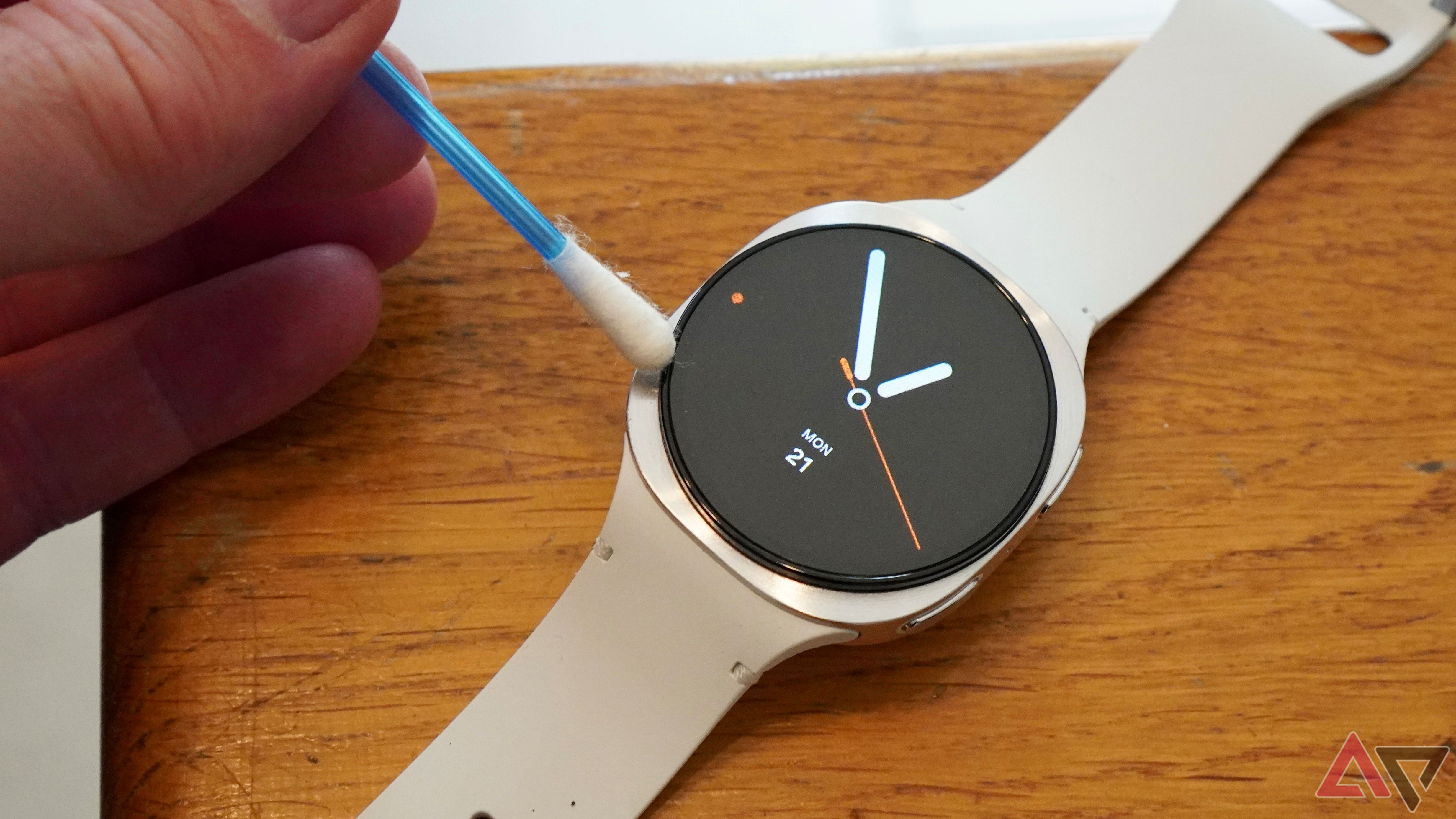 A person using a cotton swab to clean around the screen of a Samsung Galaxy Watch 8