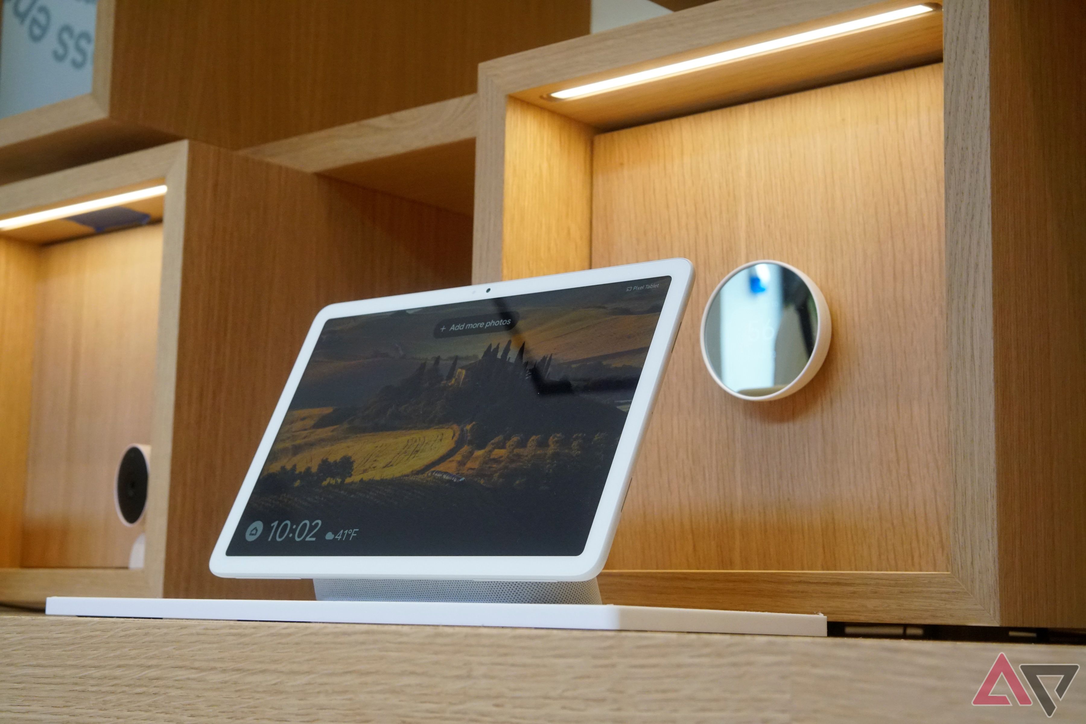 A Pixel Tablet sitting on a table with a Nest Thermostat on a wall in the background.