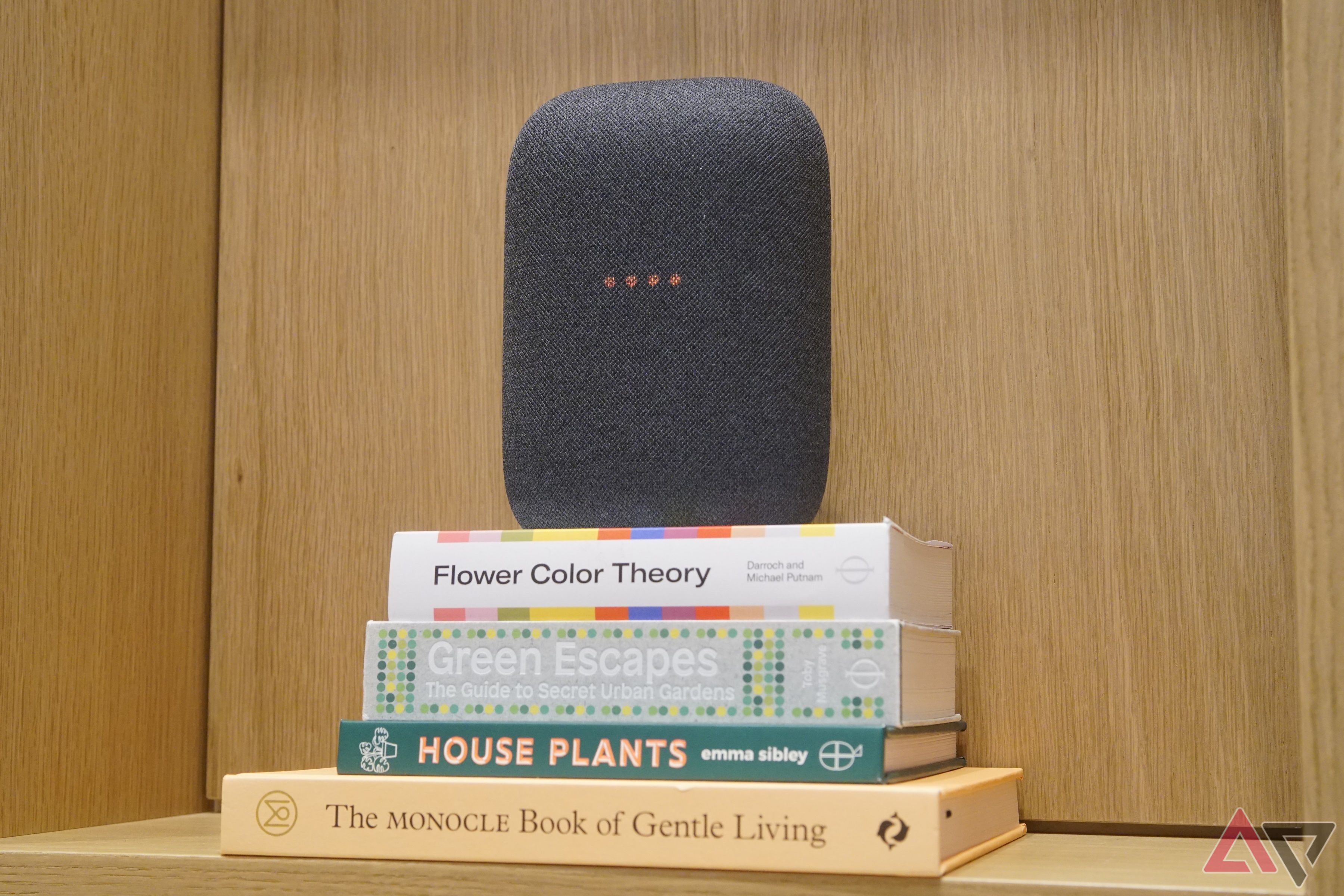 A Google Nest Audio smart speaker in gray, sat atop a stack of books.